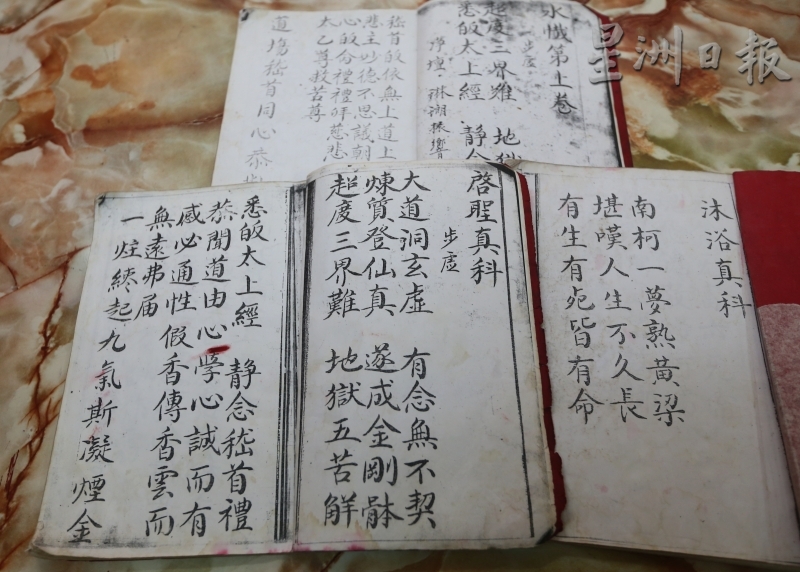 赵坤利展示在丧礼上常用的道教科本，分别为《启圣》、《沐浴》、《水忏》。（图：星洲日报）