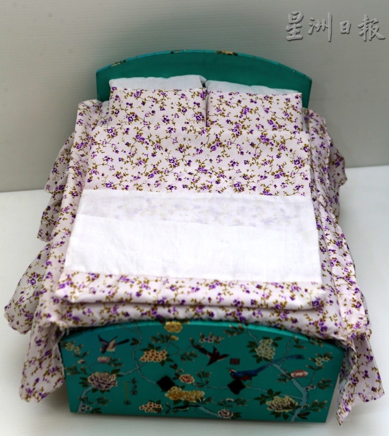 精美的月饼盒、气泡膜，加上黄丽仪亲自缝制的床单、被套及枕头，形成了以假乱真的袖珍床。（图：星洲日报）