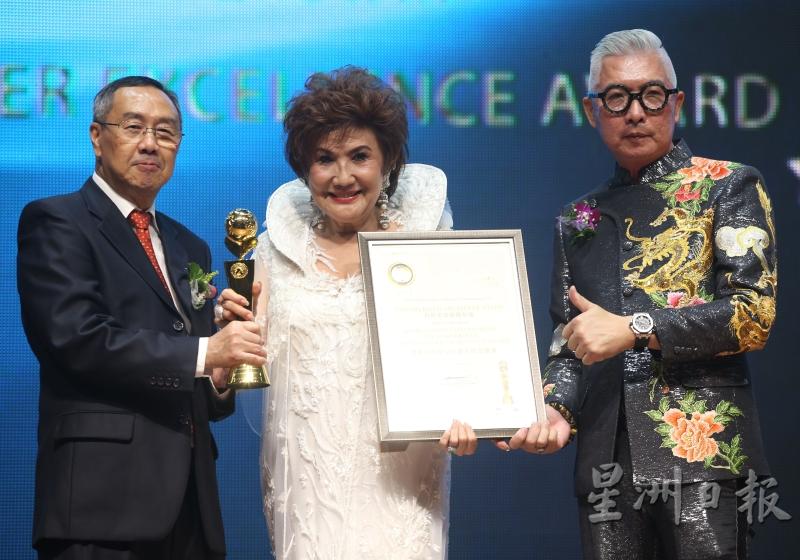 谭慧珍（中）代表女儿杨紫琼从郑可扬（左）和陈法澄手中领取世界杰出电影巨星大师卓越奖杯及奖状。