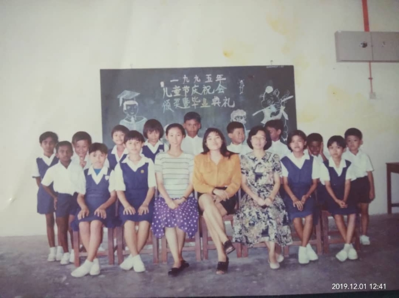 陈美容（后排左三）在手机里收着她于1995年儿童节暨毕业典礼上和老师们的合照，坐者右三为何玉华老师。
