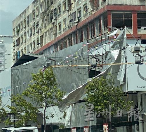 一栋空置建筑物上方，一大块锌片广告板“随风飘扬”，吓坏路上行人和驾车人士。
