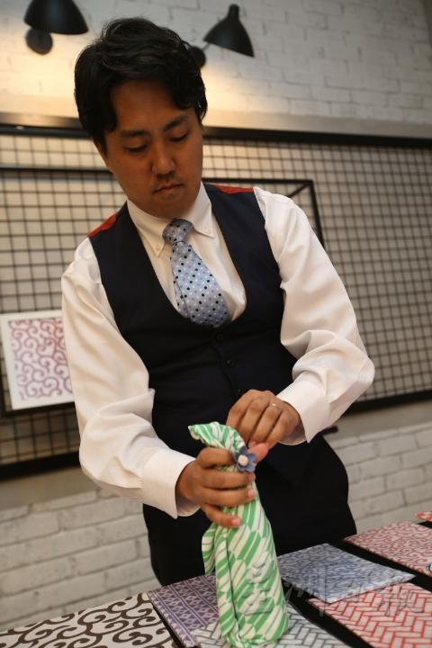 辻良岳（Yoshitake Tsuji）示范如何用手拭巾来包裹水瓶，让整体更美观和便于携带。