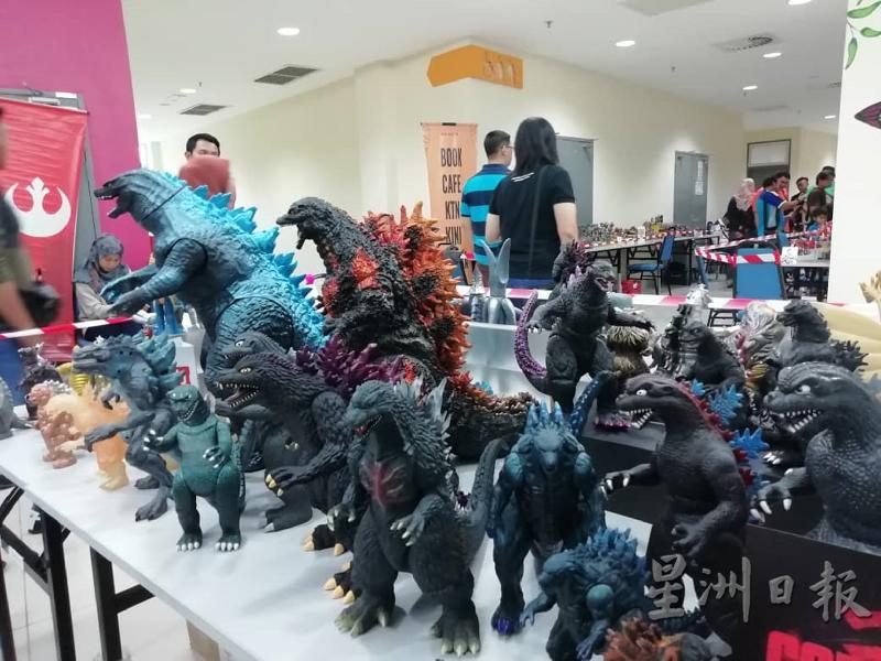 以哥斯拉怪兽为主题的展示桌上，陈列出不同时代造型的哥斯拉玩具，体积最高者大约两尺。

