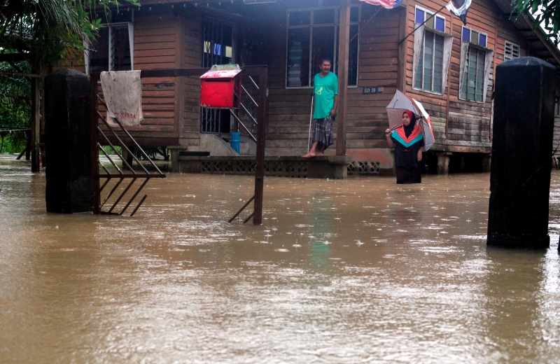 关丹甘榜古当拉扫居民阿兹哈及妻子查纳丽雅观察户外的淹水情况。