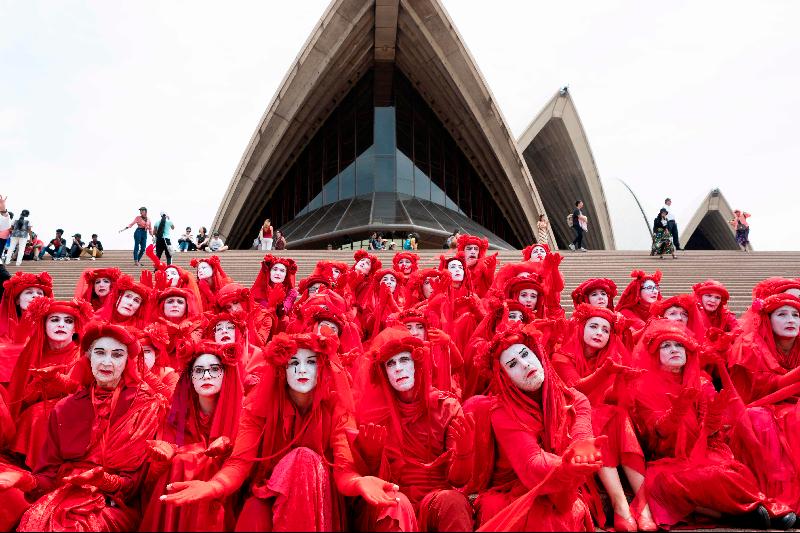 澳洲“反抗灭绝”旗下的“红色叛军”星期日身穿全红长袍、脸部白，在悉尼地标歌剧院前表演哑剧，要求对气候变迁立刻采取行动。（图：法新社）