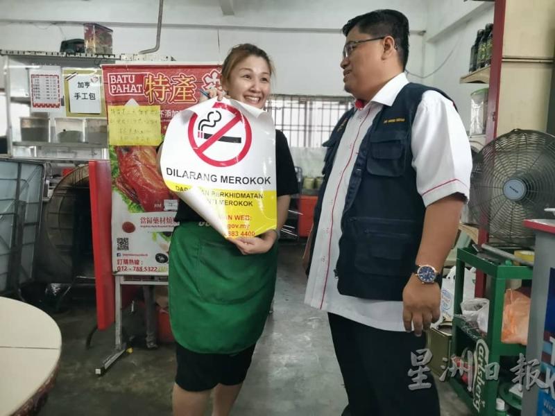 尼占（右）赠送禁烟告示牌予黄思惟，后者表示支持禁烟令并会劝告顾客不要在店内抽烟。