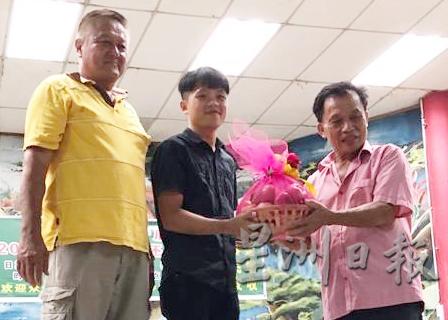代表都赖州议员邹宇晖出席宴会的劳勿新村发展官李明桉（中）从甯恩祥手中接取礼篮。左是伍开泰。