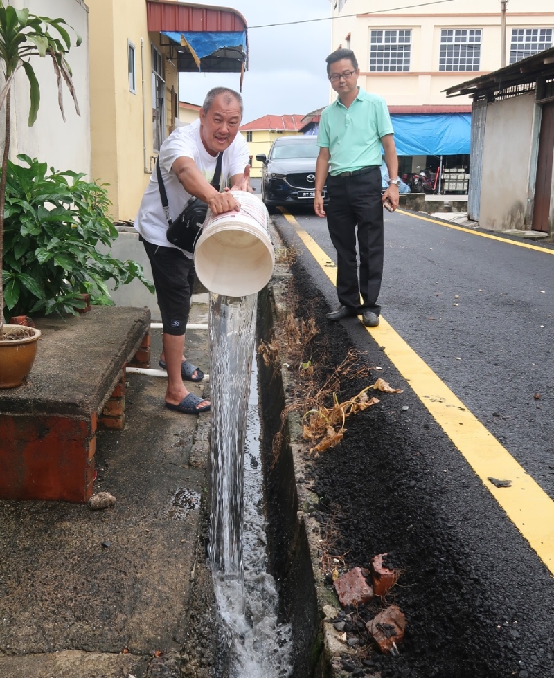 郑天生（左）用雨水冲洗店后沟渠，以减缓沟渠发出的异味，右为姚伟乐。