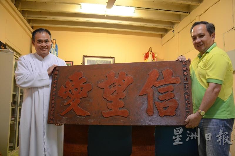 2015年，时任神父卢桂峰（左）与教友曾锦松（右）展示于1891年打造的牌匾。根据记载，该牌匾当时悬挂在打昔肚圣心天主堂旧址，随著教堂的迁址，也被拆迁到居林耶稣圣心天主堂。