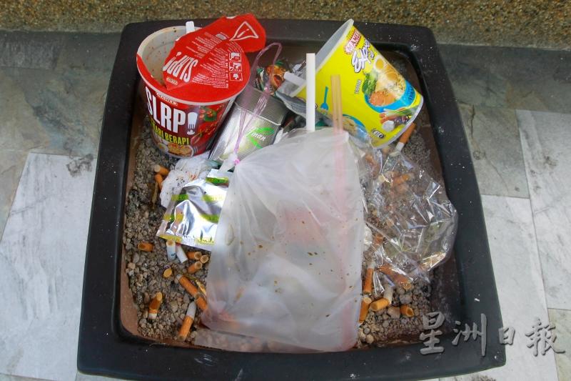 烟灰锅尺寸约一尺大，其中一个烟灰锅的底部插着许多烟蒂，但上方却堆满塑料垃圾。