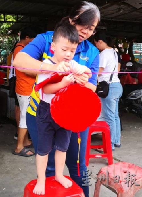 黄渼沄教导年幼的儿子把红灯笼吊挂起来。（图：星洲日报）