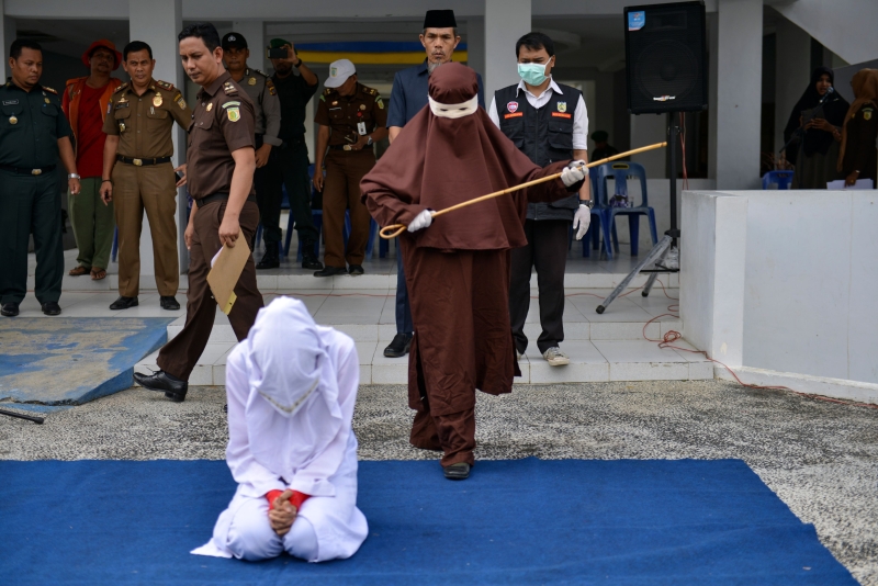 这张摄于去年12月10日的档案照片显示，印尼首名女性鞭笞行刑手在班达亚齐公开鞭打一名在酒店偷情，而被伊斯兰法庭裁定犯下道德罪的女子。（图：法新社）