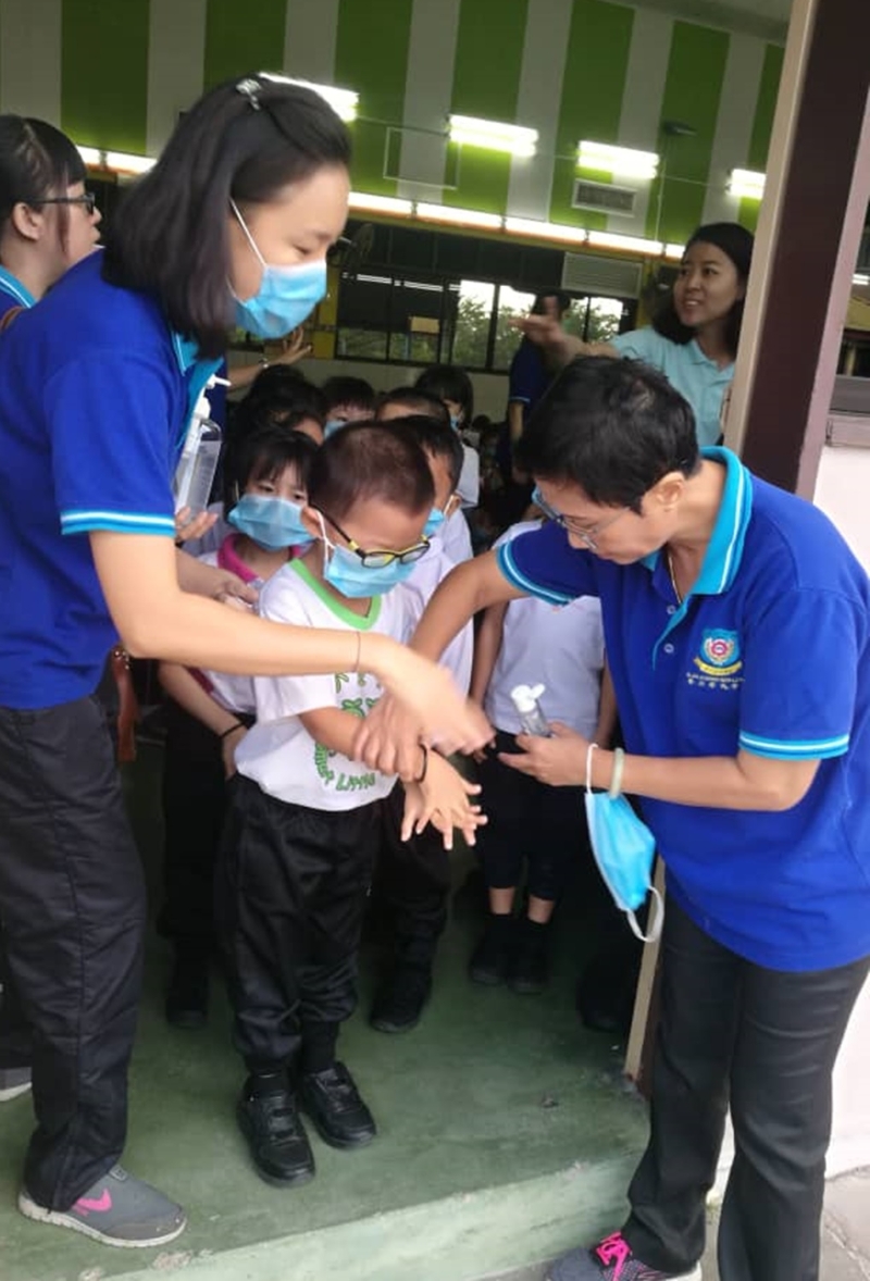 校方为了确保学生学会洗手消毒，教师手把手地教学生。右一为莫美凤。