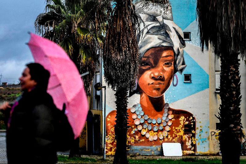 A visitor holds her umbrella close to a mural by Uruguayan artist Maria Noe during a guided visit to the Quinta do Mocho neighborhood of Sacavem outside the Portuguese capital of Lisbon. AFP