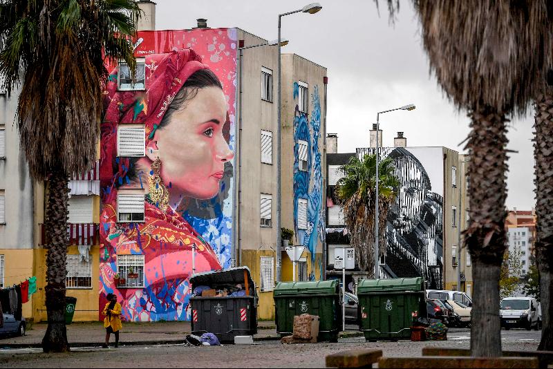 A resident walks past murals by Liberian artist Arcy (L) and Portuguese artist Huariu in Quinta do Mocho neighborhood of Sacavem outside the Portuguese capital of Lisbon. AFP