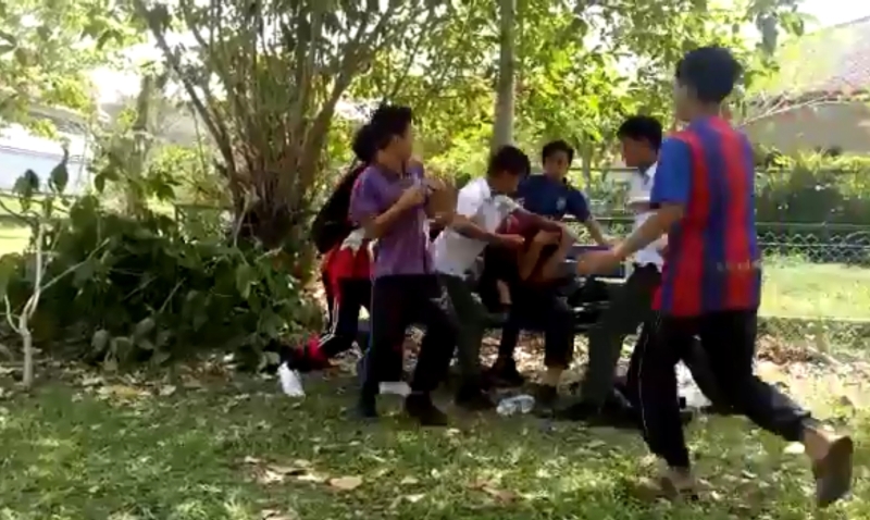 男生坐在长椅上遭男同学围殴。
