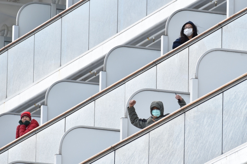 钻石公主号邮轮周四抵达横滨港码头时，一名戴口罩的乘客向媒体挥手致意。（法新社照片）
