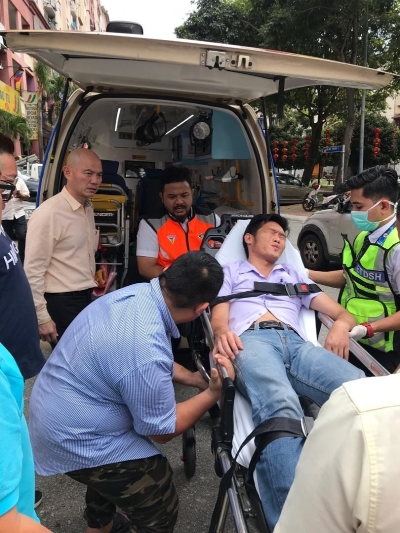 赖俊权（躺者）遭不明男子挥拳打至晕眩，并由救护车送往士拉央医院就医。左一为林立迎。