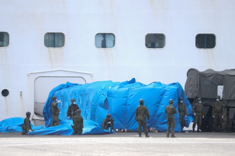 日本自卫队成员周三在横滨的码头指挥一辆军车靠近出现众多新冠肺炎确诊病例的“钻石公主号”邮轮的一个闸门。该邮轮周四又新增了44宗病例。（图：法新社）