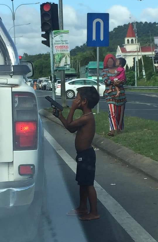光着脚和没穿衣服的男童举“枪”向停驶车辆的司机乞讨。（网络图）