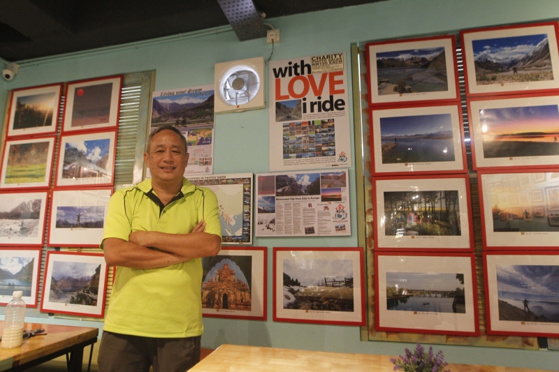 翁书发在咖啡店展示他骑脚车周游列国的照片，并开放让民众订购。