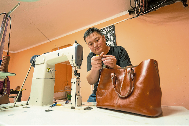 曼来峇亚曾当过皮革产品设计师，他负责剪裁、钉锤工作，索隆谷则帮忙缝制。（大马世界宣明会提供）