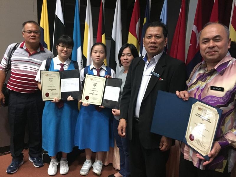 德圣中学优秀生茅嘉颖（左二）及许本迎（左三）在古晋领取2019年大马教育文凭最佳成绩奖后，与诗巫教育局局长阿赫里（右二）及校长尼古拉斯（右）合影。

