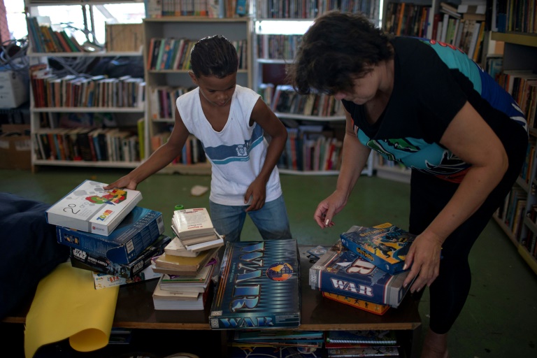 Lua Oliveira's grandmother Fatima Oliveira and a boy organize donated books at the library. AFP