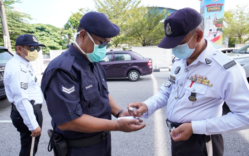 警员将公众赠送的洗手液和同僚分享，大家一同搓手消毒，做好防范措施。