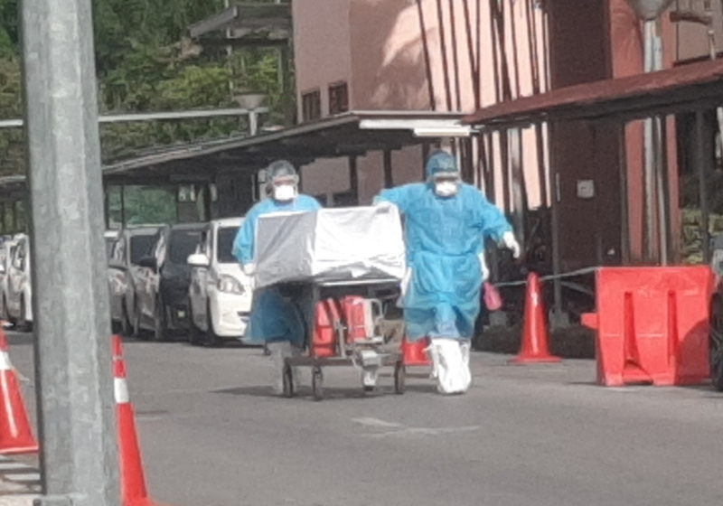 医务人员在把因感染冠病而死亡的女死者遗体推往砂中央医院太平间。