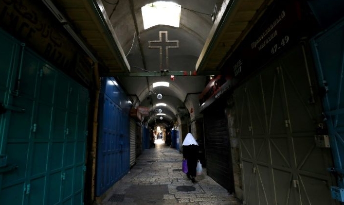 A woman walks past closed shops along a deserted alley in the Old City of Jerusalem. AFP