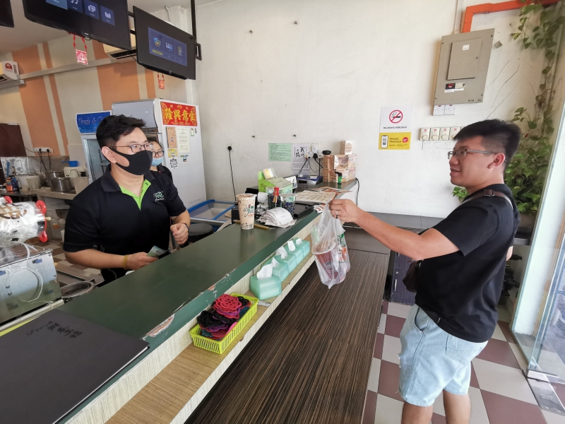 林俊雄（左）交饮料给一名顾客，生意虽锐减，但仍熟客上门。