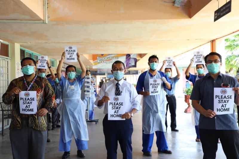 诺阿兹米（中）巡视安顺医院，并连同医护人员高举“请留在家”的纸卡，呼吁民众遵循行动管制令。