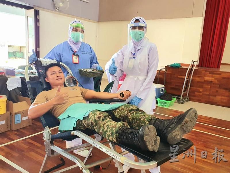 穿戴全套防护服的医护人员为响应捐血的军人打气。
