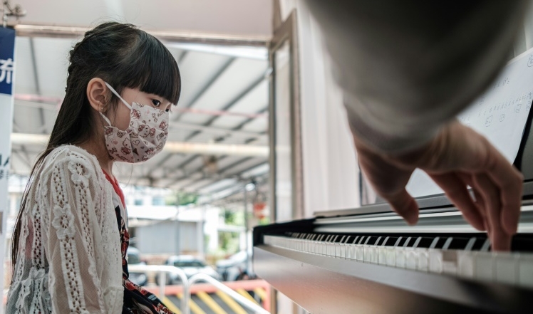 6-year-old Yoyo wears a face mask during a piano lesson in the back of a truck with teacher Evan Kam. AFP 6-year-old Yoyo wears a face mask during a piano lesson in the back of a truck with teacher Evan Kam. AFP