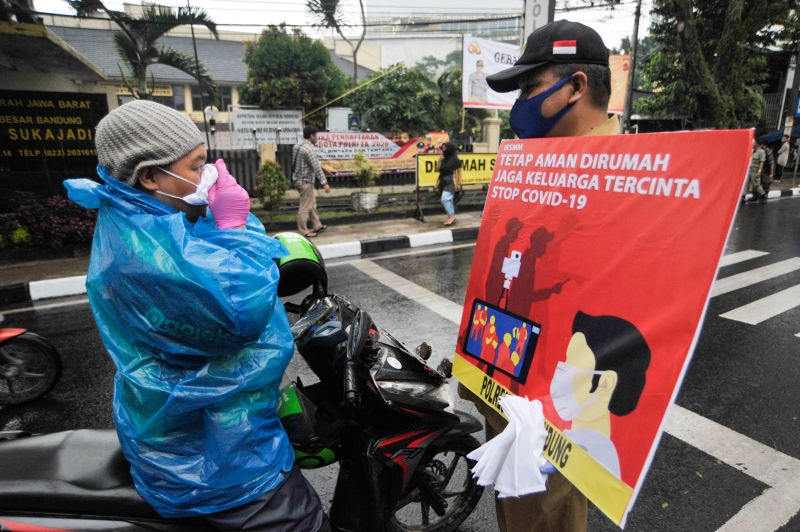  印尼将禁止民众在开斋节返乡过节，以避免加剧疫情扩散。图为西爪哇万隆 ，警察展示海报，促民众留在家里防疫。（法新社照片）