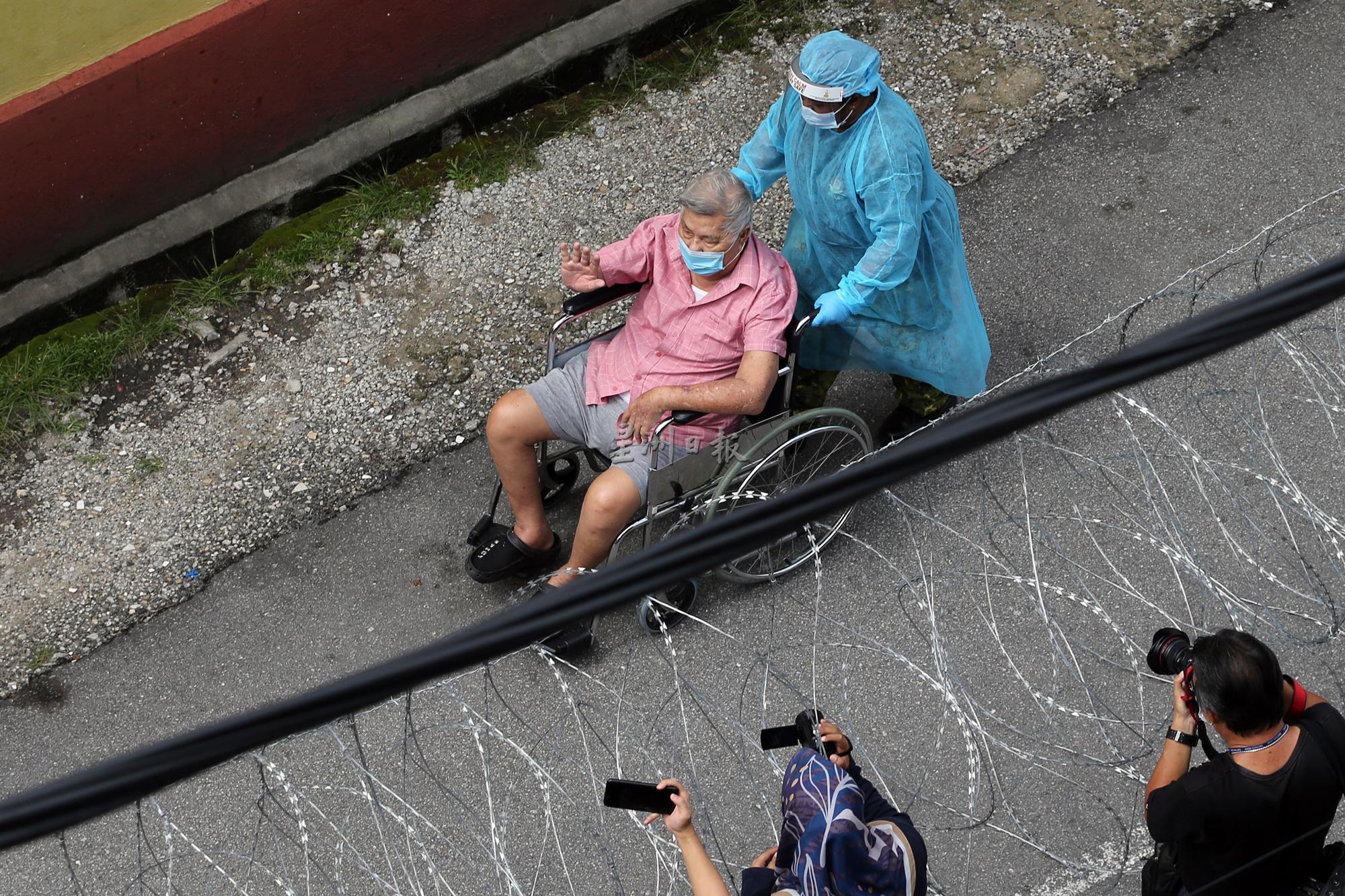 执勤人员用轮椅推着行动不便的长者，前往检疫站。