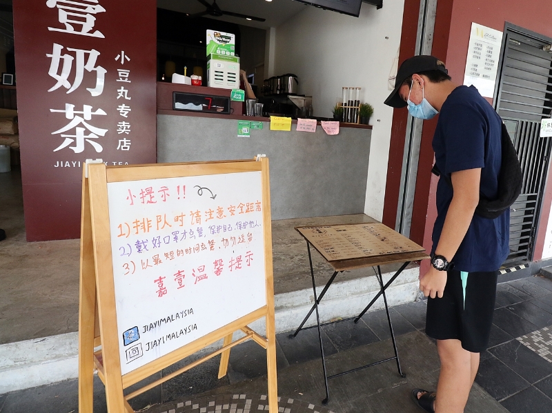 奶茶店门口立著牌子，指示前来打包的顾客点餐方式。