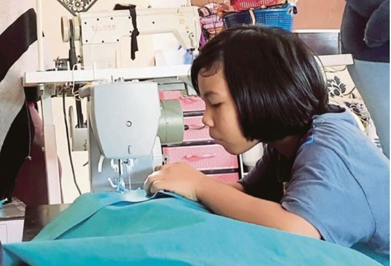 诺阿菲雅在5岁的时候已经学会裁缝技术，如今协助母亲完成130件的防护衣更引起柔河居民的瞩目。