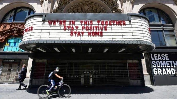 A cyclist wearing a face mask rides past the Million Dollar Theater in Los Angeles, closed due to the coronavirus pandemic. AFP
