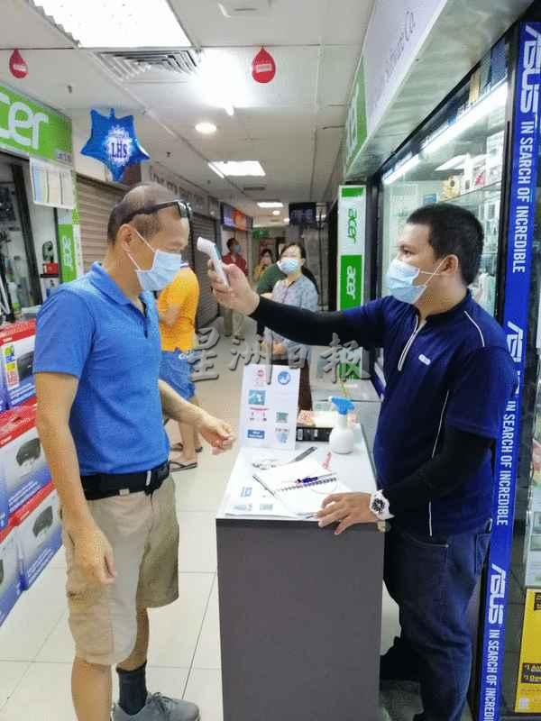 电脑店员工（右）为顾客测量体温。