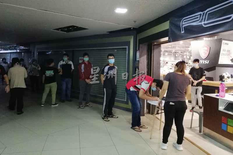 民众遵守防疫措施，在一家电脑店外排队。