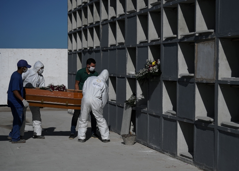 在里约热内卢的加约墓园，工作人员在抬放装有冠病死者的棺木时穿上防护装备，以降低感染风险。（图：法新社）