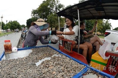 一名游客向路边的手推车摊贩购买河螺。（摄影/冯依健）