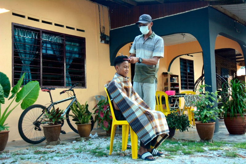 罗斯丹莫哈末(右)只用了一把剪刀及梳子，于住处户外为14岁的儿子诺依祖安哈京罗斯丹理发。