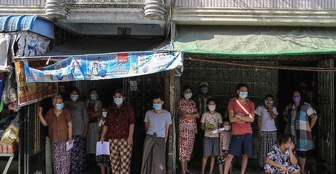 People wearing face masks wait as health workers make door-to-door health checks in Yangon. AFP