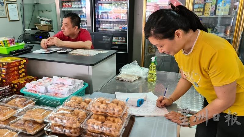 戴嫣玲（右）帮食客记录资料和体温，她表示，小贩中心开放堂食后，光顾人潮明显增加。