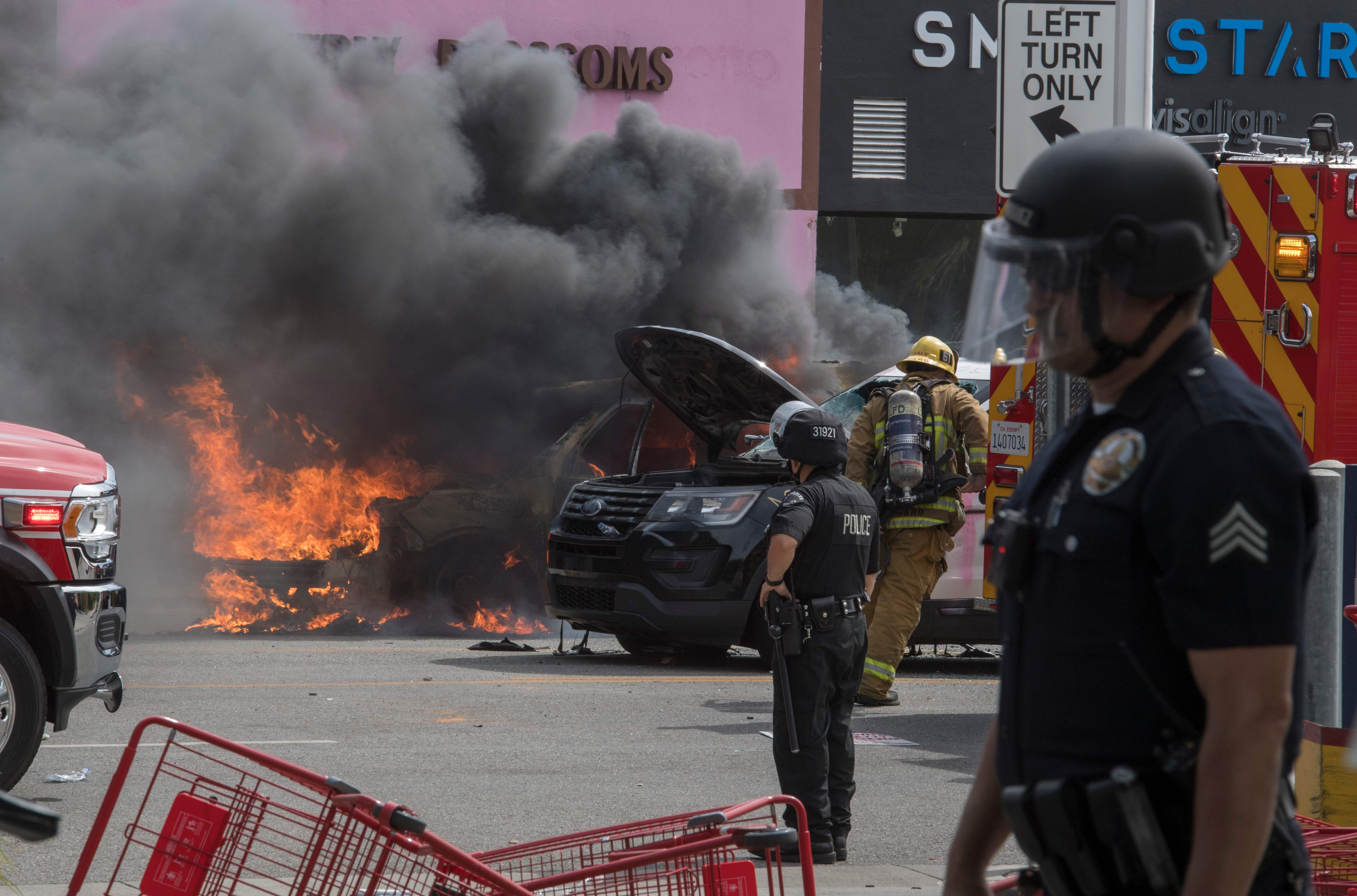 在洛杉矶，一辆警车遭暴民纵火后冒出滚滚黑烟。