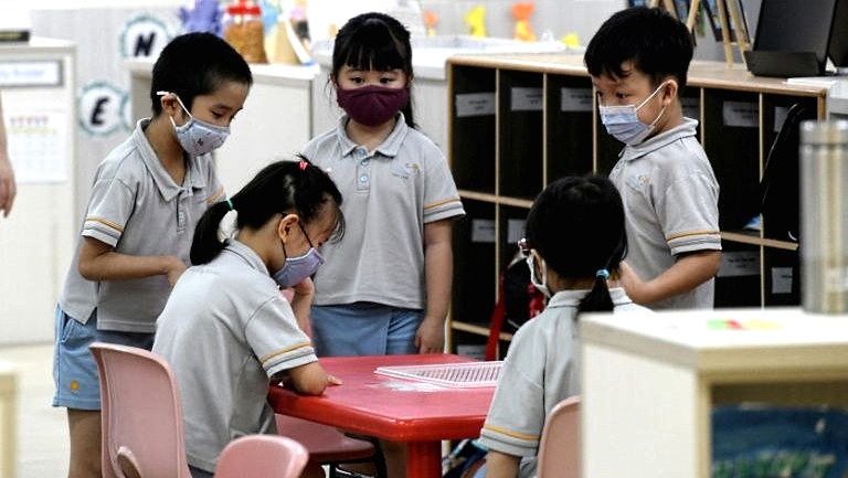 Pupils in masks gather around a table at a school. AFP