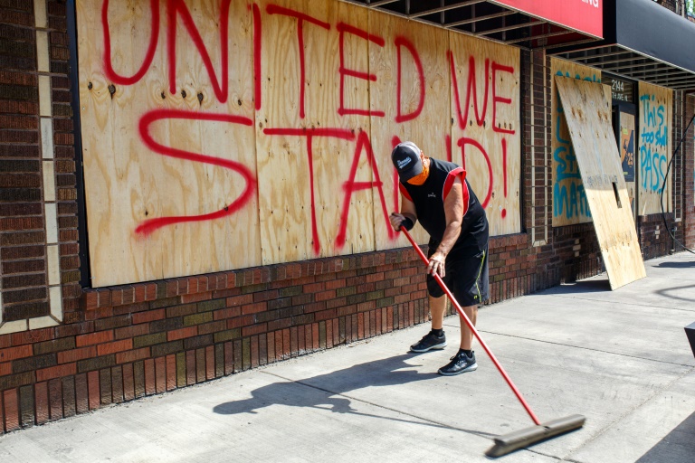 Tom Bernard cleans up debris in front of his barber shop in Minneapolis after a night of protests. AFP